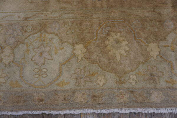 Muted, high-pile rug detail showing floral patterns in brown, beige, and sage over distressed wood flooring.