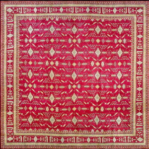 Square deep red rug with intricate cream and gold geometric patterns and multi-paneled borders.