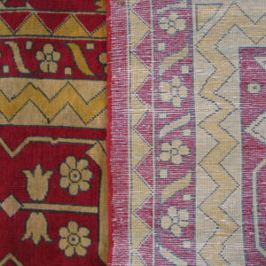 Detail of a folded rug showing red and gold high-pile floral patterns next to a flat geometric woven backing.