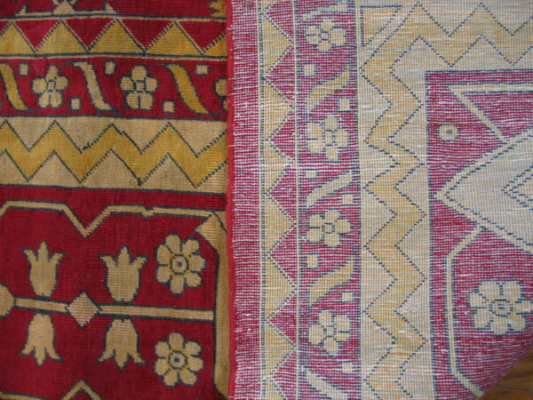Detail of a folded rug showing red and gold high-pile floral patterns next to a flat geometric woven backing.
