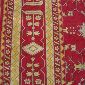 Deep red rug detail featuring intricate yellow geometric and floral border patterns on wood flooring.
