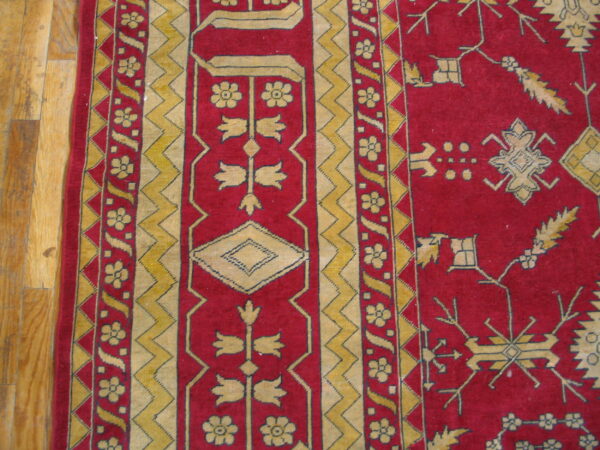 Deep red rug detail featuring intricate yellow geometric and floral border patterns on wood flooring.