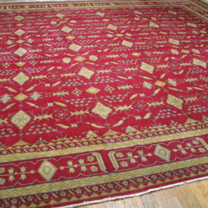 Crimson rug featuring detailed repeating yellow geometric and stylized floral designs on a wood floor.