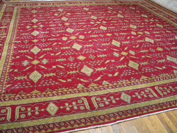Crimson rug featuring detailed repeating yellow geometric and stylized floral designs on a wood floor.