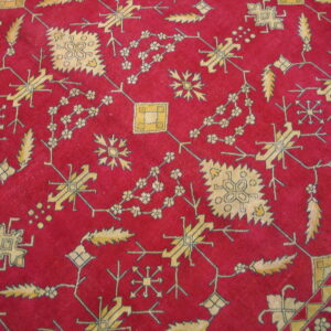 Close-up of a red rug featuring intricate yellow and beige geometric and stylized floral motifs.