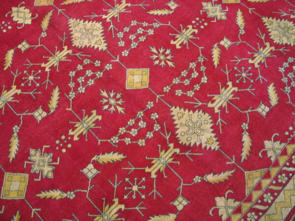 Close-up of a red rug featuring intricate yellow and beige geometric and stylized floral motifs.