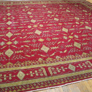 A deep crimson rug with gold traditional patterns and borders is laid over brown wood planks.
