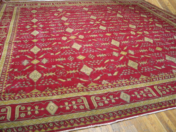 A deep crimson rug with gold traditional patterns and borders is laid over brown wood planks.
