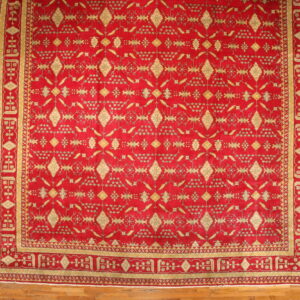 Red and gold patterned area rug with a wide border displayed on light brown wood flooring.