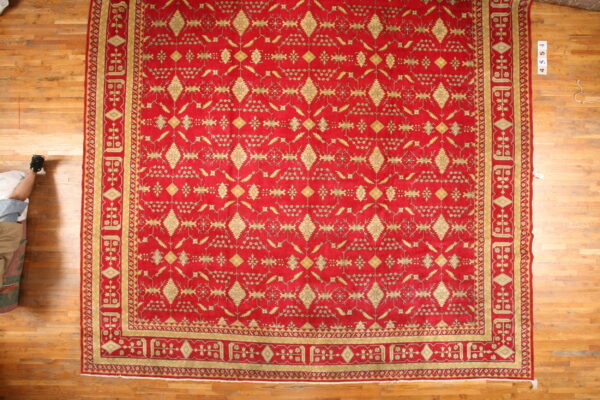 Red and gold patterned area rug with a wide border displayed on light brown wood flooring.