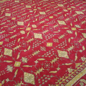 Red low-pile rug with a dense pattern of yellow geometric and stylized floral figures and visible borders.