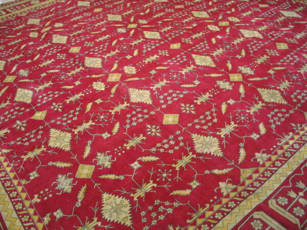Red low-pile rug with a dense pattern of yellow geometric and stylized floral figures and visible borders.