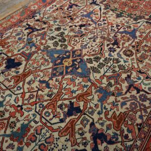 Angled view of a patterned rug with cream ground, red, and blue motifs on worn wood planks.
