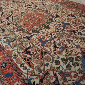 Traditional low-pile rug with a detailed cream, red, and blue pattern resting on wood flooring.