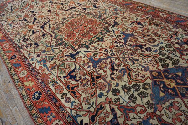Traditional low-pile rug with a detailed cream, red, and blue pattern resting on wood flooring.