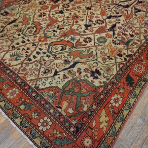 Cream field rug with rust border and complex stylized designs resting on weathered hardwood flooring.