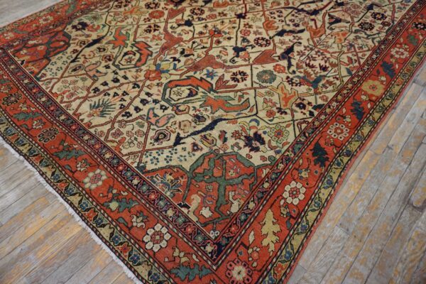 Cream field rug with rust border and complex stylized designs resting on weathered hardwood flooring.