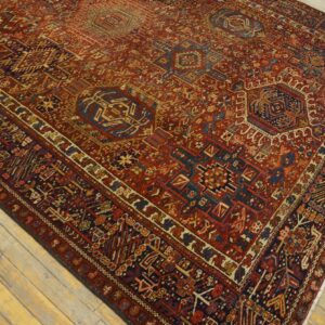 Detailed red tribal rug with blue geometric patterns and medallions lying on light plank hardwood.
