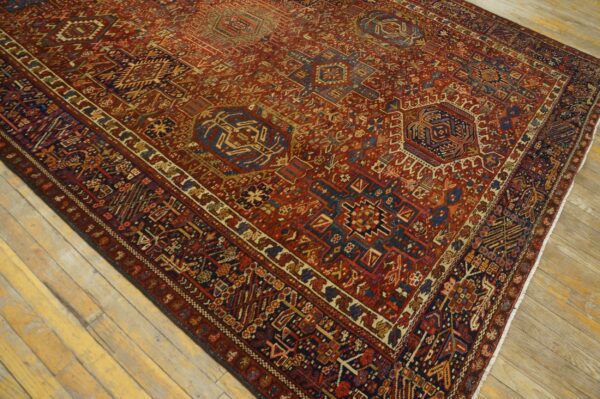 Detailed red tribal rug with blue geometric patterns and medallions lying on light plank hardwood.