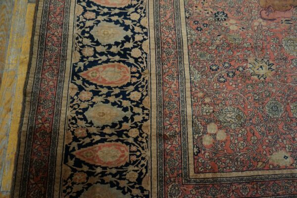 Close-up of a floral rug with navy blue border panels and a salmon pink field on wooden flooring.