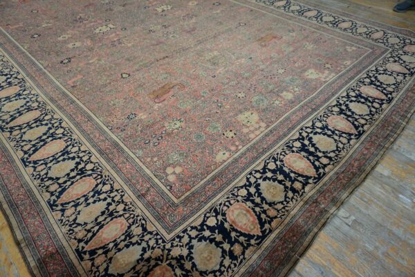 Ornate pink and blue rug featuring a dense floral pattern and wide paisley border on distressed wood floors.