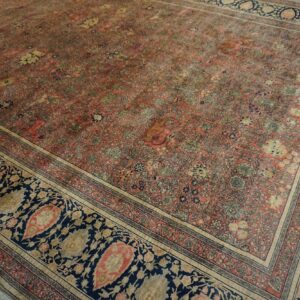 Faded pink rug featuring an intricate floral motif bordered by bold navy blue paisley designs.