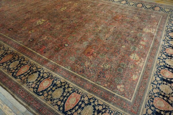 Faded pink rug featuring an intricate floral motif bordered by bold navy blue paisley designs.