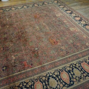 Faded pink rug with dense botanical patterns and a dark blue border rests on distressed wood planks.