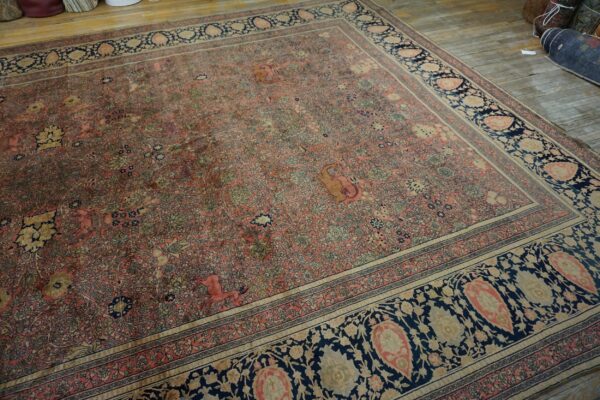 Faded pink rug with dense botanical patterns and a dark blue border rests on distressed wood planks.
