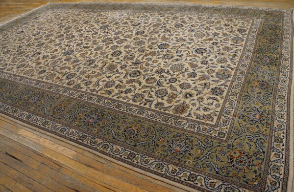 Cream floral rug with blue accents and a wide sage border sits on distressed hardwood planks.