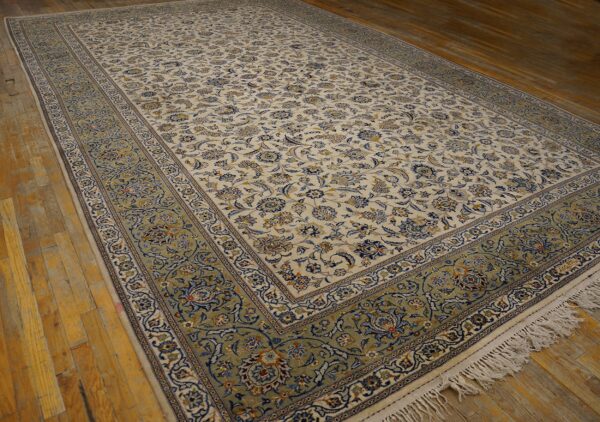 Cream and blue floral rug with a wide green border lying on distressed hardwood planks.