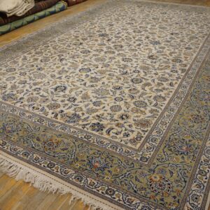 Cream traditional rug with a dense blue floral design and wide pale green border on wood flooring.