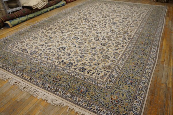 Cream traditional rug with a dense blue floral design and wide pale green border on wood flooring.