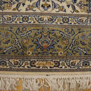 Traditional ivory, sage green, and blue floral rug borders with fringe resting on a light wood floor.