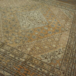 Low-pile beige and tan medallion rug with complex floral patterns on weathered wooden floors.