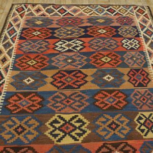 Flatweave rug with banded geometric patterns in navy, rust, brown, and beige on rustic wood flooring.