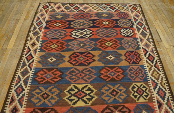 Flatweave rug with banded geometric patterns in navy, rust, brown, and beige on rustic wood flooring.