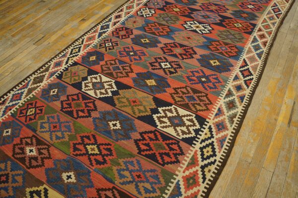 Geometric flatweave runner with red, blue, and earth-toned patterns resting on worn yellow wooden floorboards.