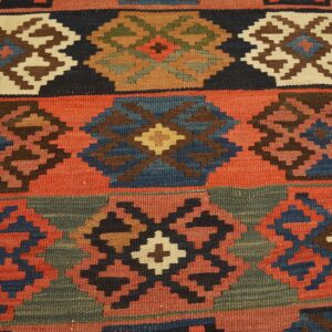 A coarse, flatweave rug displays multicolored geometric designs including navy, rust, brown, and muted green.