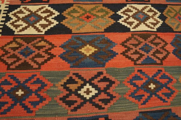 A coarse, flatweave rug displays multicolored geometric designs including navy, rust, brown, and muted green.