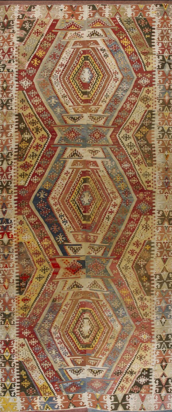 Colorful geometric flatweave rug with repeating vertical diamond medallions in red, yellow, blue, and beige.