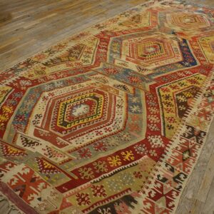 Multicolored flatweave rug featuring geometric repeating designs in red, blue, and gold on wood planks.