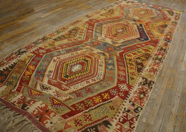 Multicolored flatweave rug featuring geometric repeating designs in red, blue, and gold on wood planks.