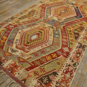 Geometric low-pile rug with central hexagons in red, yellow, and blue on rustic hardwood flooring.