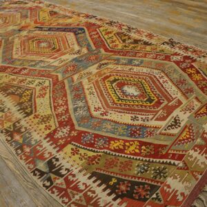 Flat-woven rug with complex geometric medallions in red, blue, cream, and yellow on wood planks.