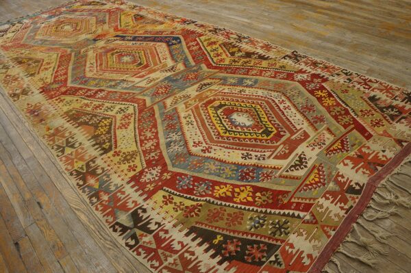 Flat-woven rug with complex geometric medallions in red, blue, cream, and yellow on wood planks.
