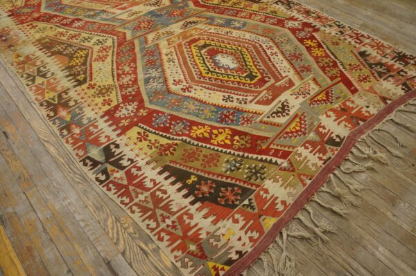 Geometric flatweave rug featuring a large medallion in vivid red, yellow, and blue on distressed wood planks.