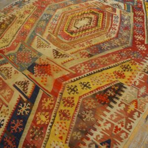 Flatweave rug with nested geometric patterns in red, yellow, blue, and cream on rustic wood flooring.