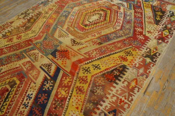 Flatweave rug with nested geometric patterns in red, yellow, blue, and cream on rustic wood flooring.