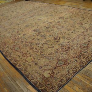 Oversized beige rug with detailed red and blue floral motifs rests on worn hardwood planks.